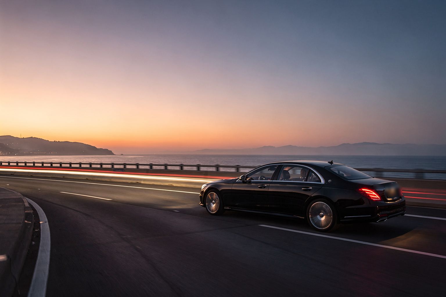 A black sedan on a coastal motorway at sunset