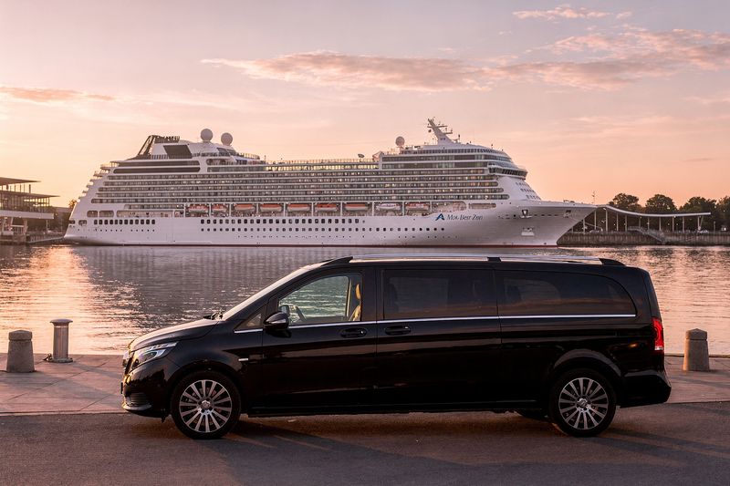 A black people mover on the quay beside a docked cruise ship at sunrise