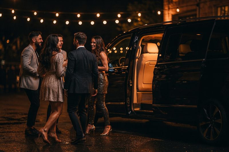 Friends in party clothes beside a black minibus at night under string lights
